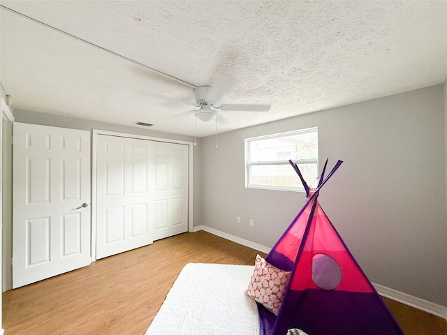 unfurnished bedroom with wood finished floors, baseboards, ceiling fan, a closet, and a textured ceiling