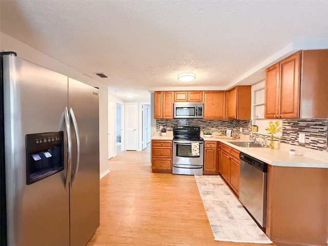 kitchen featuring stainless steel appliances, a sink, light wood finished floors, light countertops, and a textured ceiling