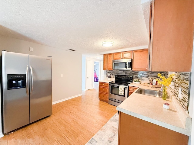 kitchen featuring appliances with stainless steel finishes, a sink, light wood-type flooring, light countertops, and decorative backsplash