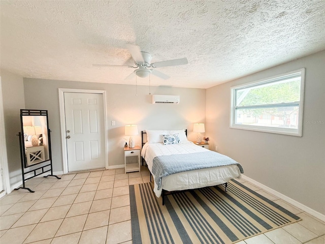 bedroom with a wall unit AC, light tile patterned flooring, baseboards, and a textured ceiling