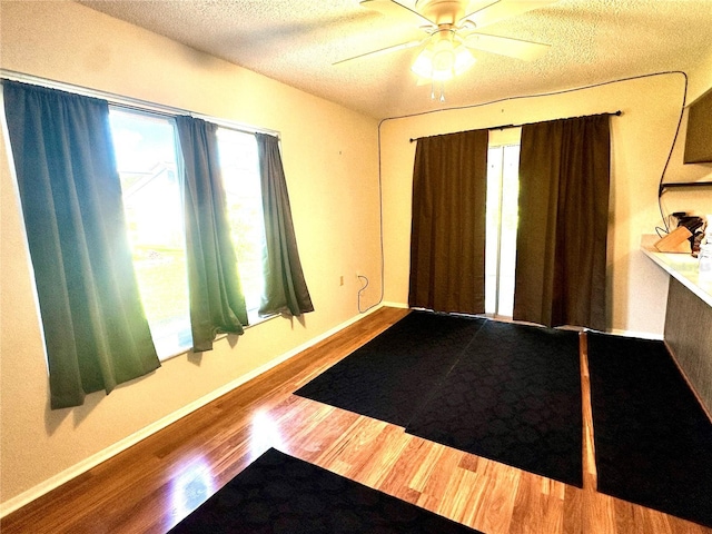 foyer entrance with baseboards, a textured ceiling, ceiling fan, and wood finished floors