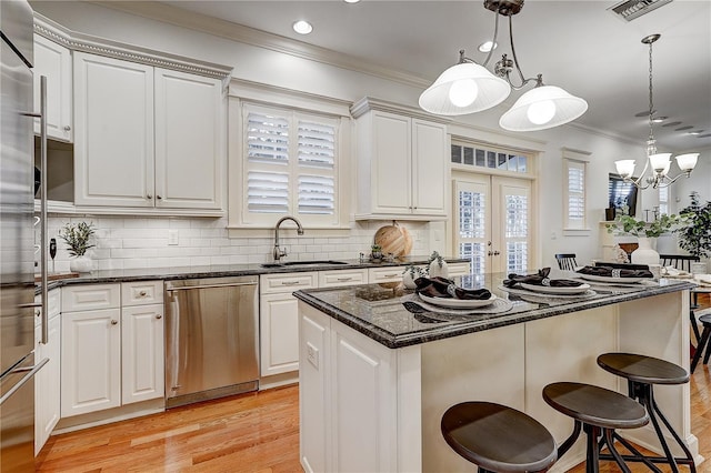 kitchen featuring white cabinets, stainless steel dishwasher, decorative light fixtures, a kitchen island, and sink