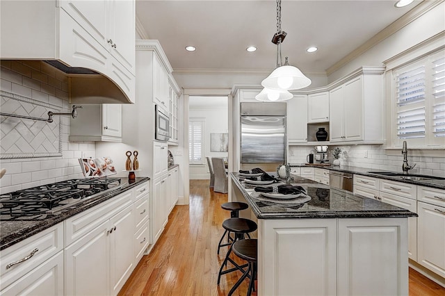 kitchen with hanging light fixtures, a kitchen island, built in appliances, sink, and white cabinets