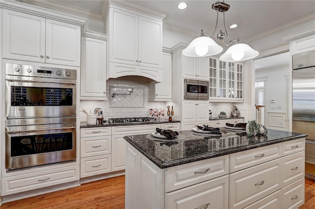 kitchen with built in appliances, light hardwood / wood-style flooring, hanging light fixtures, crown molding, and white cabinetry