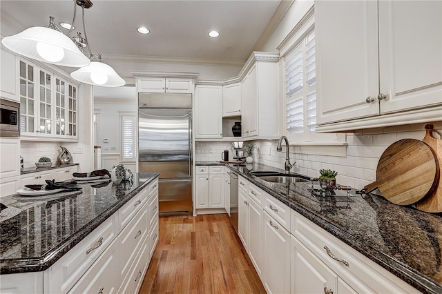 kitchen with built in appliances, decorative light fixtures, sink, white cabinetry, and dark stone countertops