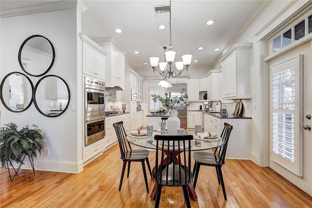 dining room featuring sink, ornamental molding, light wood-type flooring, and an inviting chandelier