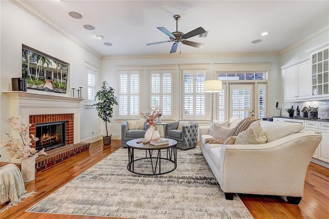 living room with hardwood / wood-style flooring, a brick fireplace, crown molding, and ceiling fan