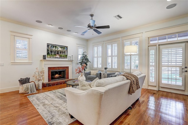 living room with plenty of natural light, crown molding, a brick fireplace, and light hardwood / wood-style flooring