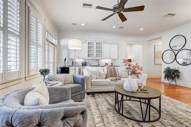 living room featuring ceiling fan, light hardwood / wood-style flooring, sink, and crown molding