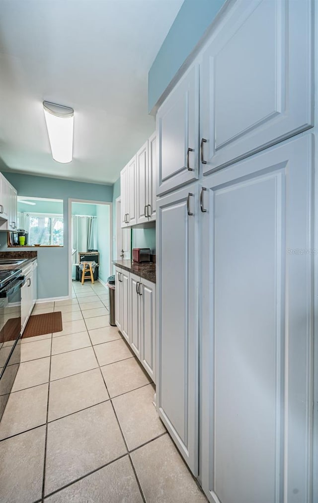 kitchen with white cabinetry, light tile patterned flooring, and black range oven