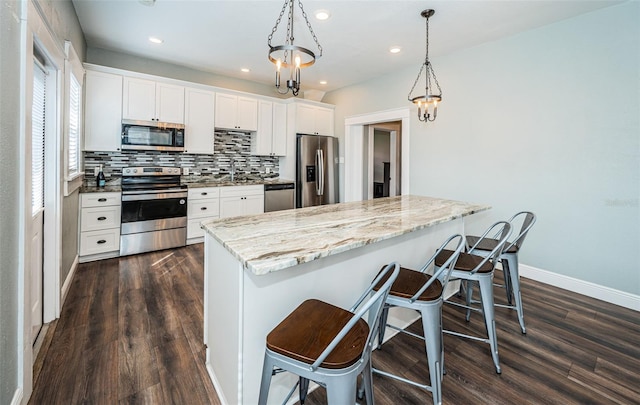 kitchen with appliances with stainless steel finishes, dark hardwood / wood-style flooring, hanging light fixtures, white cabinetry, and a notable chandelier