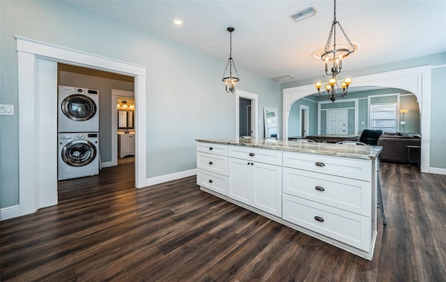 kitchen with dark hardwood / wood-style floors, stacked washing maching and dryer, decorative light fixtures, white cabinets, and light stone counters