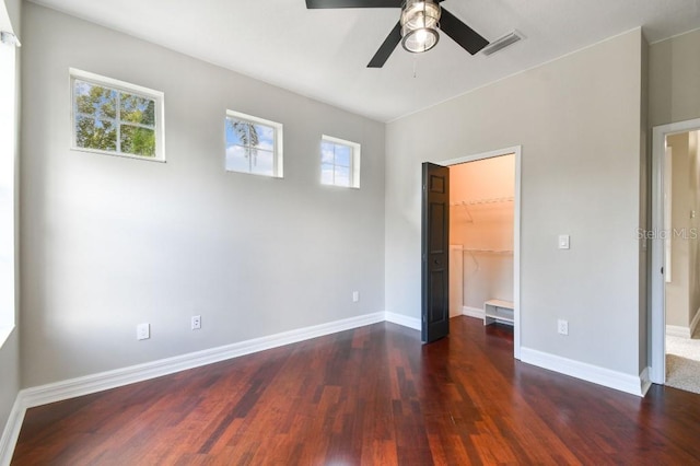 unfurnished bedroom with dark wood-type flooring, ceiling fan, multiple windows, and a walk in closet