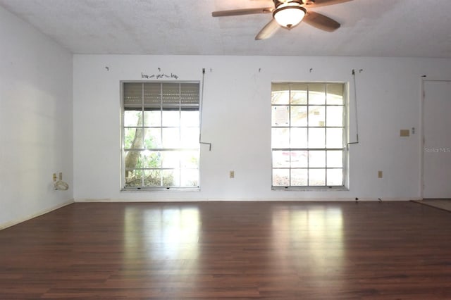 empty room with a wealth of natural light, dark wood-type flooring, a textured ceiling, and ceiling fan