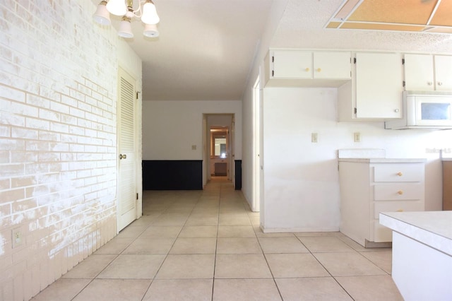 kitchen featuring an inviting chandelier, white cabinetry, brick wall, and light tile patterned floors