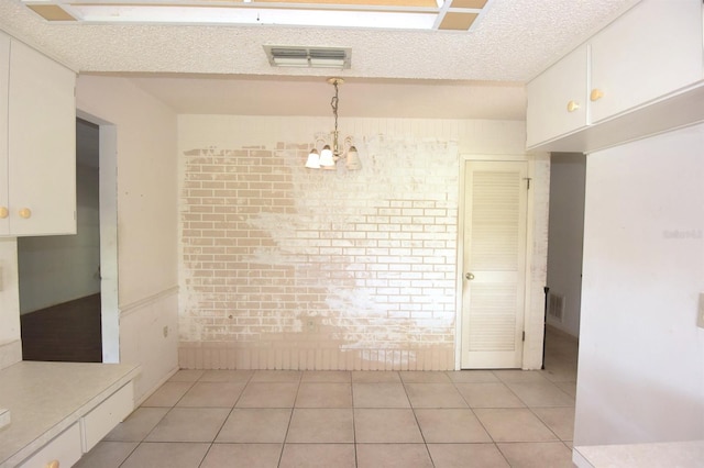 unfurnished dining area with a textured ceiling, light tile patterned flooring, and an inviting chandelier