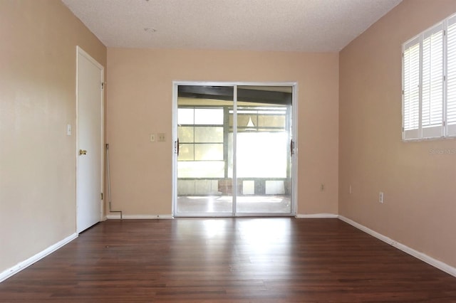 empty room with dark wood-type flooring, a healthy amount of sunlight, and a textured ceiling