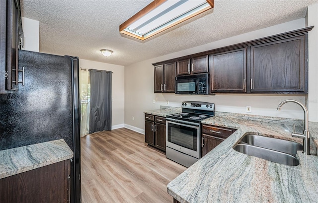 kitchen featuring dark brown cabinets, light stone countertops, light wood-type flooring, black appliances, and sink