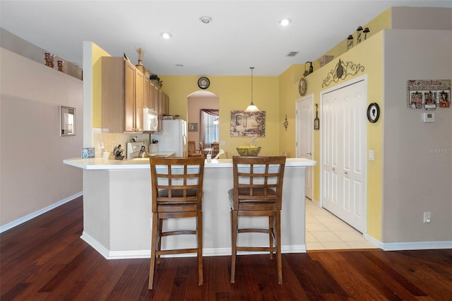 kitchen featuring white appliances, light brown cabinetry, light wood-type flooring, kitchen peninsula, and hanging light fixtures