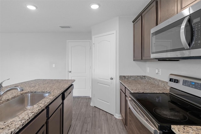 kitchen with sink, stainless steel appliances, light stone counters, dark brown cabinets, and light wood-type flooring