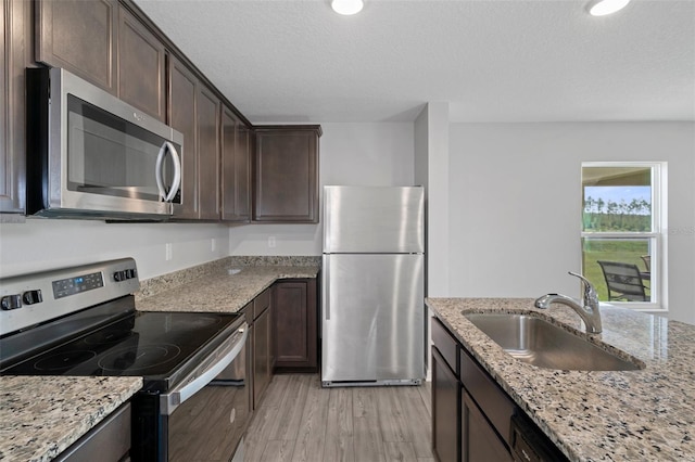 kitchen featuring sink, light hardwood / wood-style flooring, light stone countertops, a textured ceiling, and stainless steel appliances