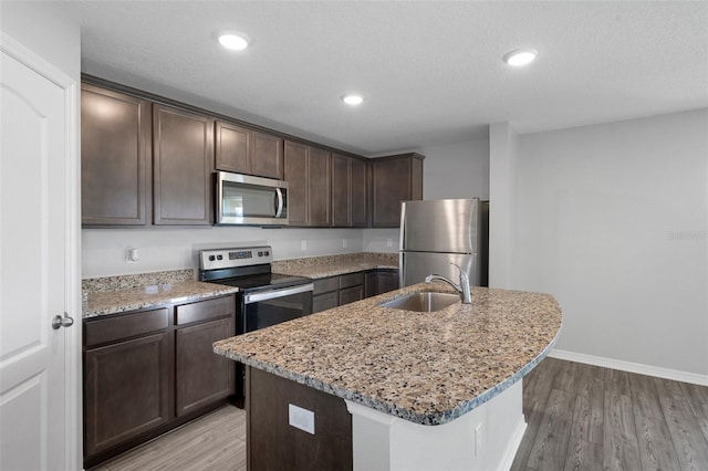 kitchen featuring light stone countertops, appliances with stainless steel finishes, sink, a center island with sink, and light hardwood / wood-style floors