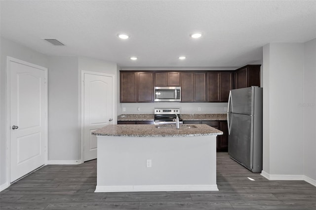 kitchen with dark hardwood / wood-style floors, dark brown cabinets, an island with sink, and appliances with stainless steel finishes