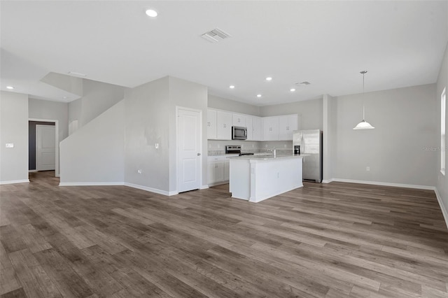 kitchen with hanging light fixtures, hardwood / wood-style floors, a center island with sink, white cabinets, and appliances with stainless steel finishes