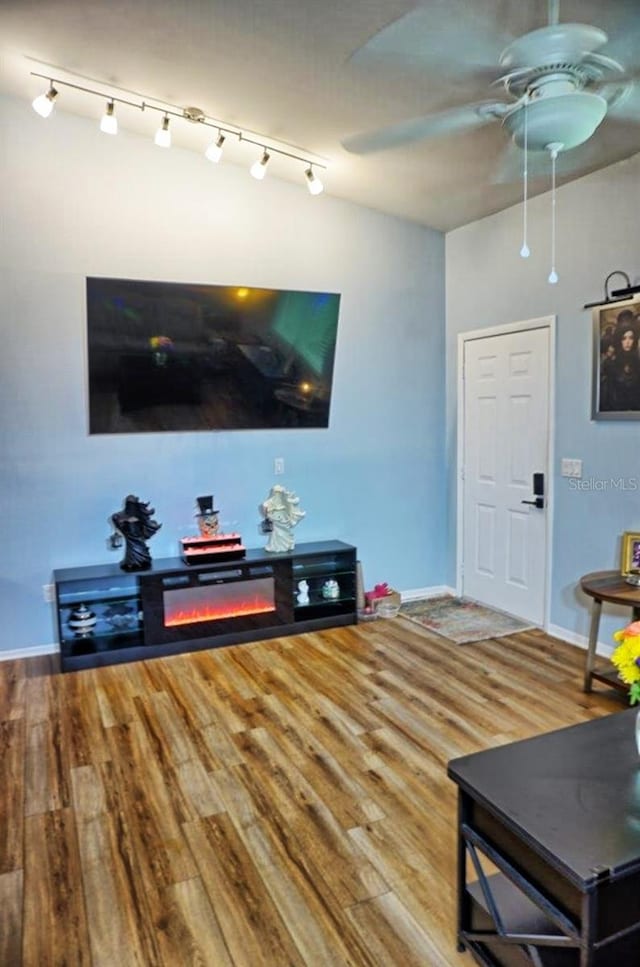 living area featuring track lighting, wood finished floors, a ceiling fan, and baseboards
