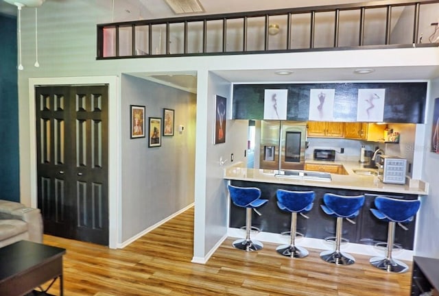 kitchen with light wood-style flooring, a breakfast bar area, stainless steel fridge with ice dispenser, baseboards, and a peninsula