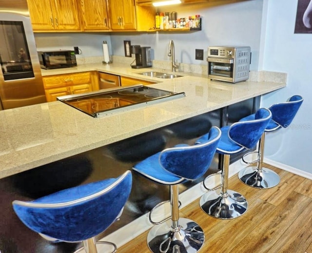 kitchen featuring wood finished floors, light stone counters, a breakfast bar area, smart refrigerator, and a sink
