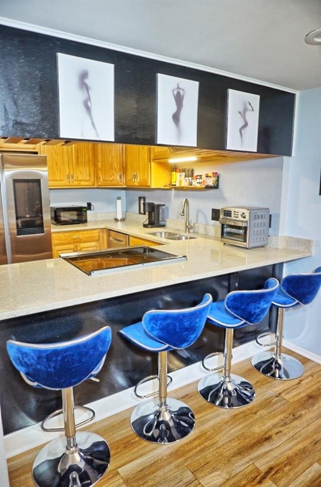 kitchen with sink, stainless steel refrigerator, a breakfast bar area, and wood-type flooring