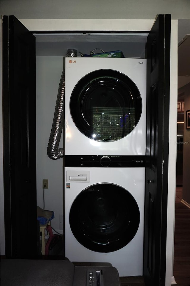 clothes washing area featuring stacked washing maching and dryer, wood finished floors, and laundry area