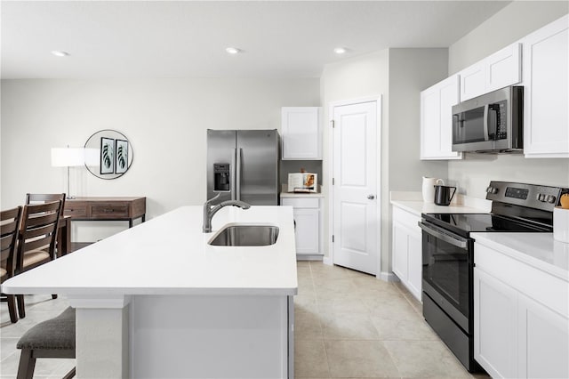 kitchen featuring an island with sink, stainless steel appliances, sink, light tile patterned floors, and white cabinets