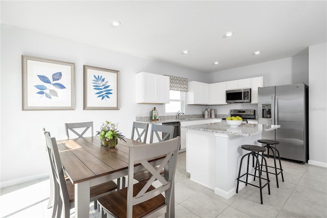 kitchen featuring light stone countertops, appliances with stainless steel finishes, light tile patterned flooring, a kitchen island, and white cabinets