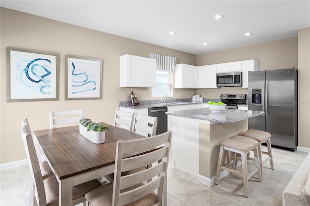 kitchen with a center island, light tile patterned flooring, white cabinetry, appliances with stainless steel finishes, and light stone counters