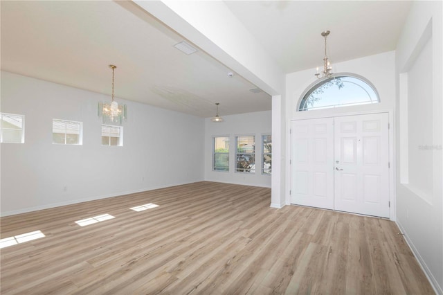 foyer with a notable chandelier, a wealth of natural light, light wood-type flooring, and a high ceiling