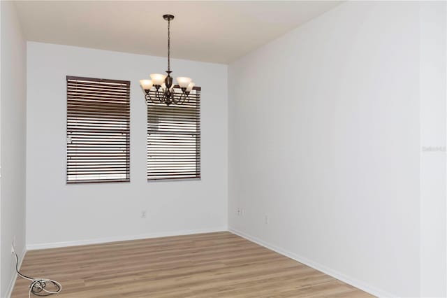 empty room with light hardwood / wood-style floors and an inviting chandelier