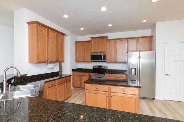 kitchen with stainless steel appliances, dark stone countertops, sink, a textured ceiling, and light hardwood / wood-style floors