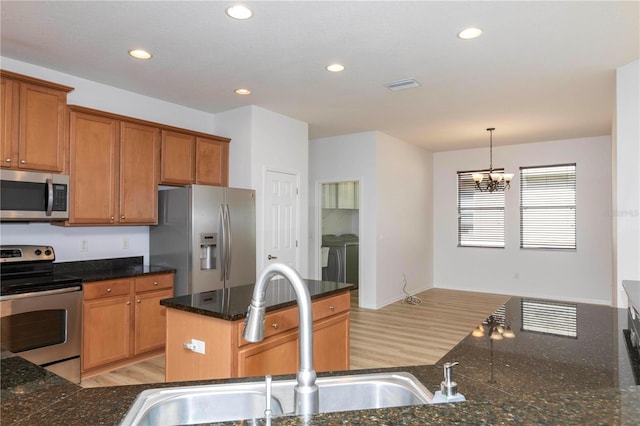 kitchen with appliances with stainless steel finishes, sink, light wood-type flooring, washing machine and clothes dryer, and an inviting chandelier