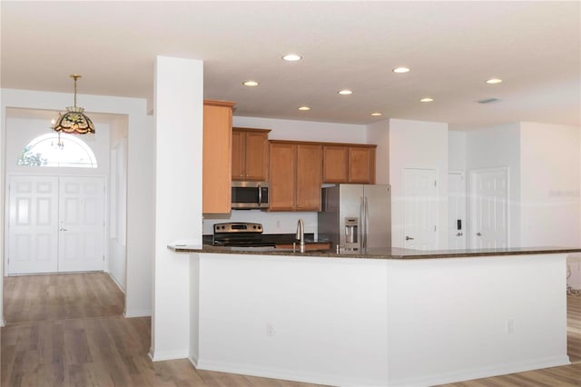 kitchen with dark stone countertops, pendant lighting, stainless steel appliances, and light wood-type flooring