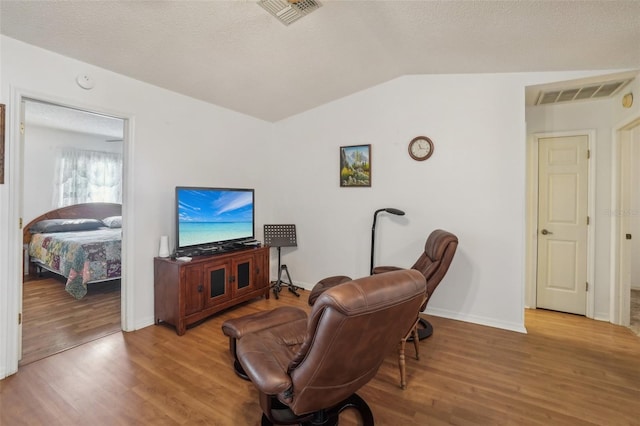 living room featuring visible vents, wood finished floors, and vaulted ceiling