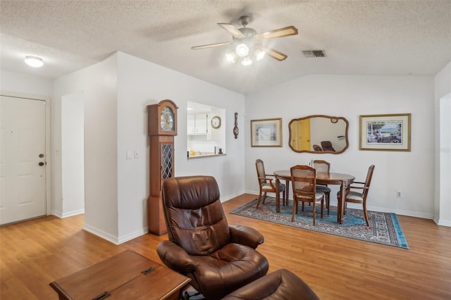 dining space featuring visible vents, light wood-style floors, a textured ceiling, a ceiling fan, and vaulted ceiling