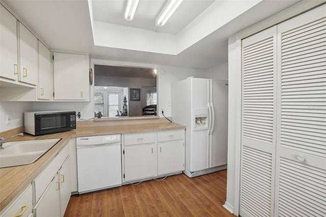 kitchen with a sink, light wood-style floors, white appliances, light countertops, and a tray ceiling