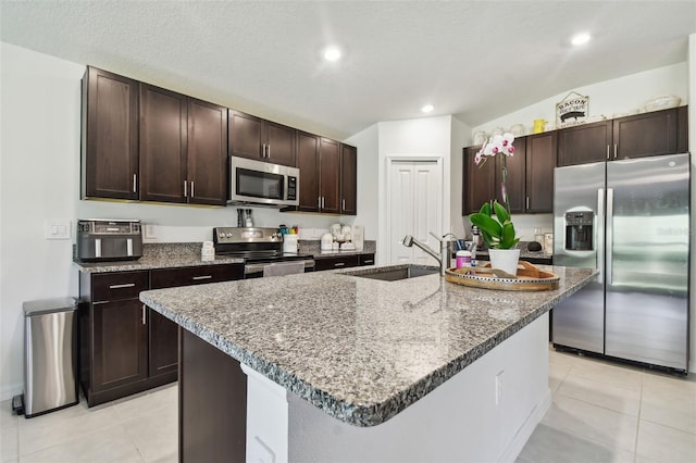 kitchen featuring a kitchen island with sink, stainless steel appliances, sink, and dark brown cabinetry