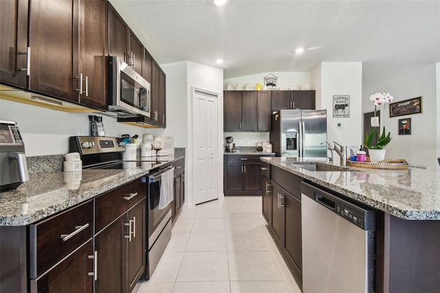 kitchen with light stone counters, a center island with sink, stainless steel appliances, light tile patterned floors, and sink