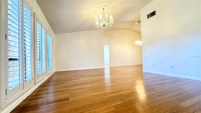 empty room with a textured ceiling, hardwood / wood-style flooring, lofted ceiling, and a notable chandelier