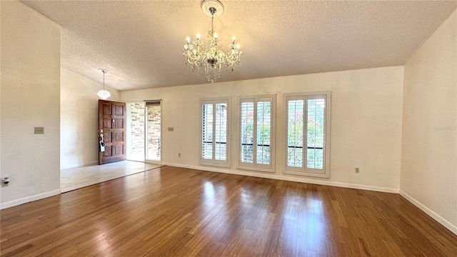 spare room featuring a textured ceiling, dark hardwood / wood-style flooring, vaulted ceiling, and an inviting chandelier