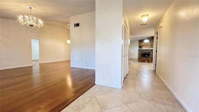 tiled empty room with vaulted ceiling, an inviting chandelier, and a stone fireplace