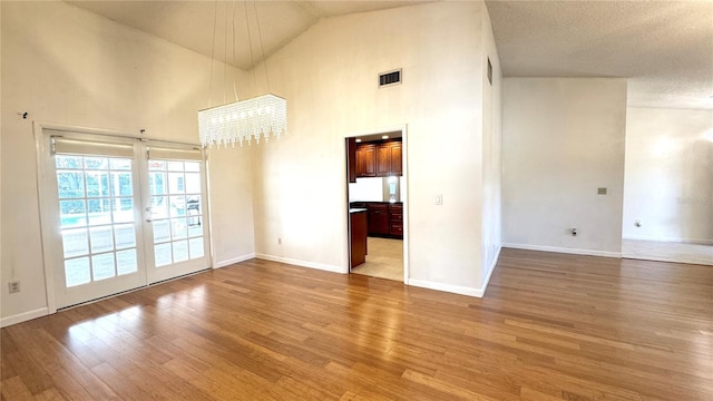 empty room with high vaulted ceiling, wood-type flooring, and an inviting chandelier